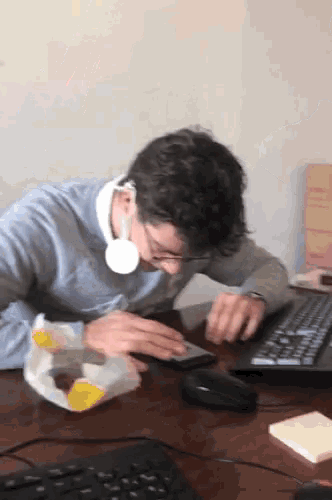 a man wearing headphones sits at a desk using a laptop