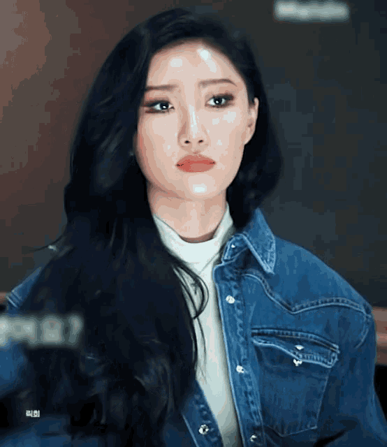 a woman with long black hair is wearing a denim jacket and a white turtleneck