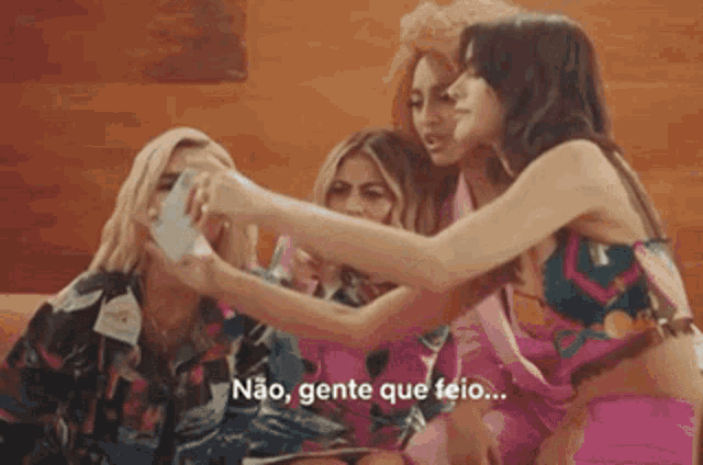 a woman is sitting at a table looking at her phone and says `` não , gente que feio ... '' .