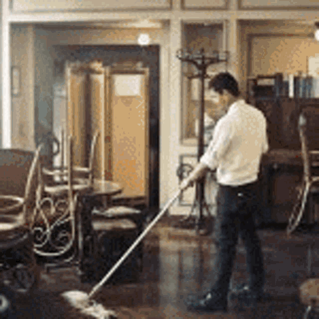 a man is mopping the floor of a room with tables and chairs .