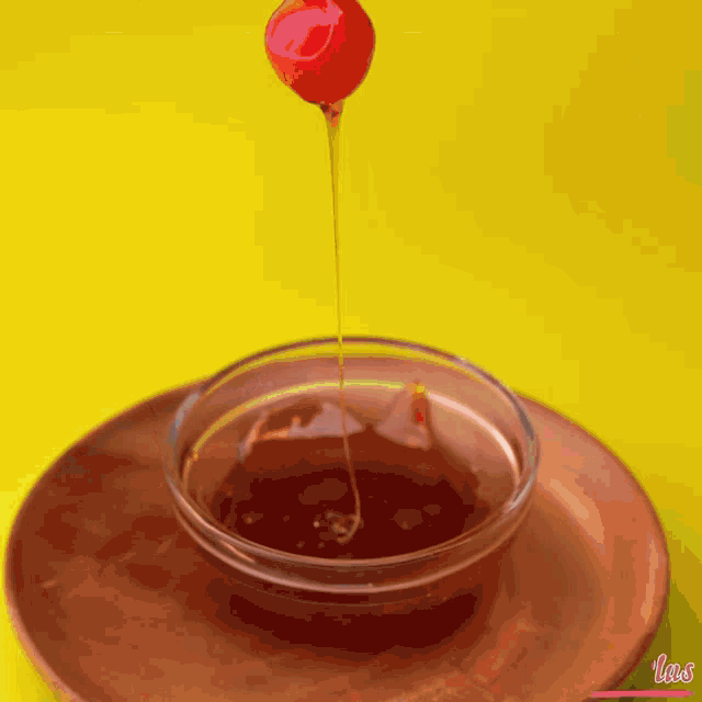 a person holds a cherry on a stick over a bowl of liquid