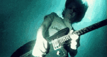 a man in a white shirt is playing a guitar in the dark .