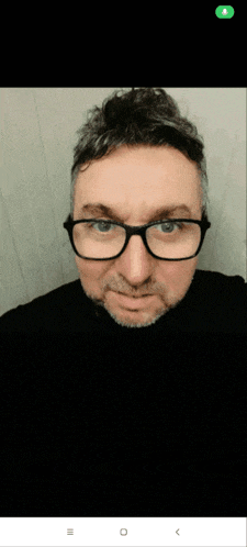 a man wearing glasses and a blue sweater taking a selfie