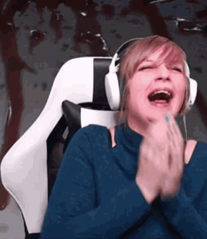 a woman wearing headphones laughs while sitting in a gaming chair