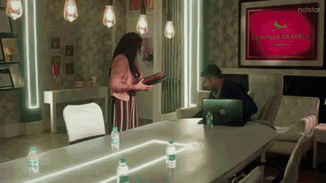 a man sits at a desk with a laptop and a woman stands in front of a sign for dharma travels