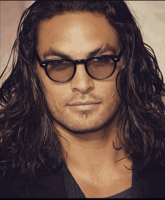 a man with long hair wearing glasses and a black jacket