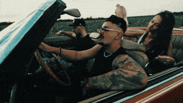 a man with a tattoo on his arm is driving a convertible car