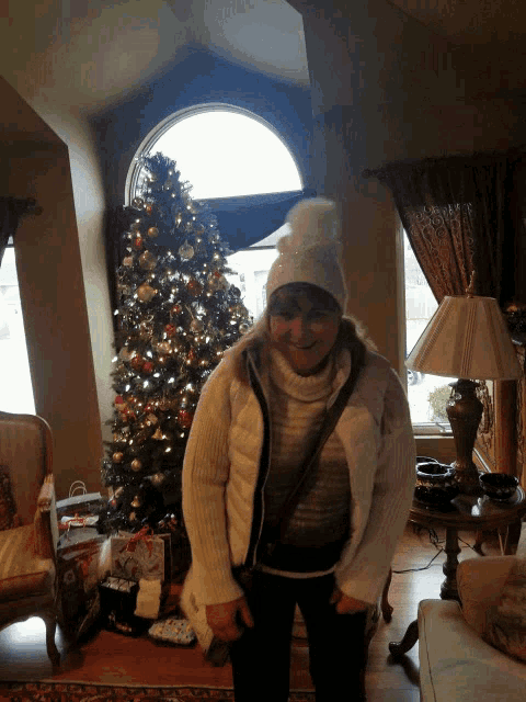 a woman stands in front of a christmas tree in a living room