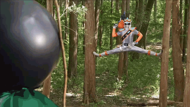 a man in a superhero costume is jumping in the air in the woods