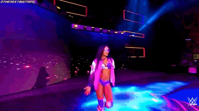 a woman in a pink jacket and blue shorts is dancing on a stage with a w logo in the background