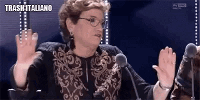 a woman is giving a high five in front of a microphone while wearing glasses and a black and gold jacket .