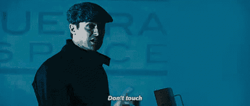 a man in a hat is standing in front of a blue wall and says do n't touch