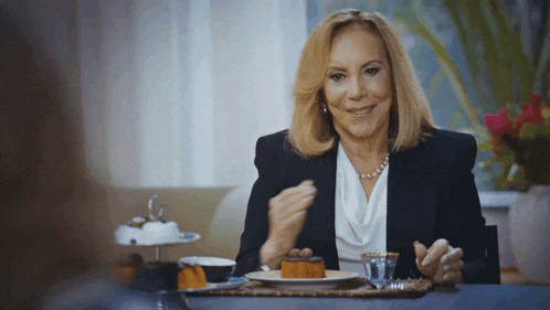 a woman in a black jacket sits at a table with a plate of food