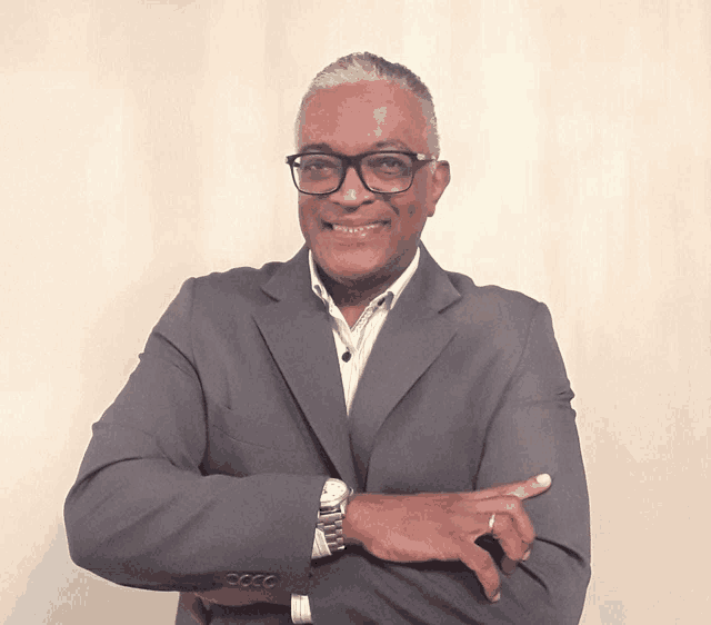 a man wearing a suit and glasses is smiling with his arms crossed