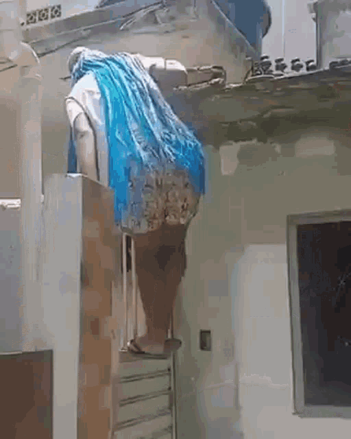 a woman is hanging from the roof of a building with a blue scarf .