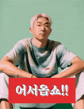 a man in a tie dye shirt sits in front of a green background with a red sign that says !!