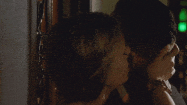 a man and a woman are kissing in a dark room with a green light behind them