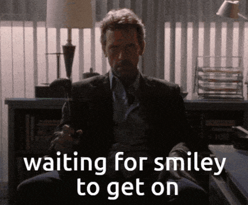 a man in a suit and tie is sitting in front of a sign that says " waiting for smiley to get on "