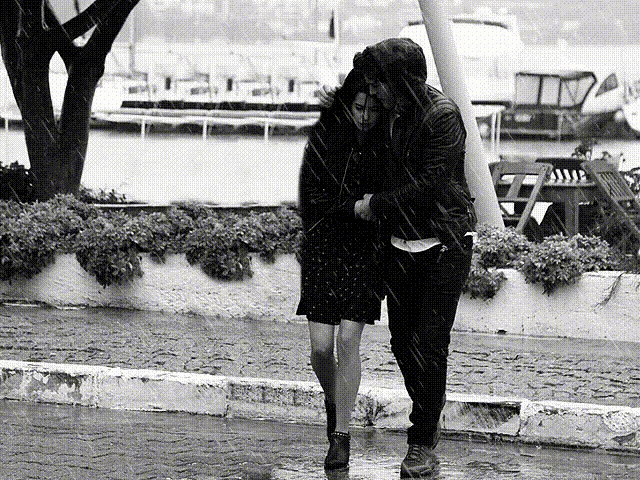 a black and white photo of a man and a woman hugging in the rain