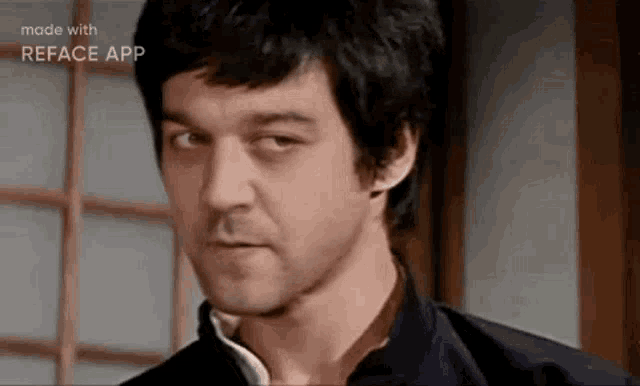 a man with black hair and a beard is making a funny face while standing in front of a window .