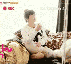 a woman is sitting on a couch with a cup of coffee in front of a recorder that says rec