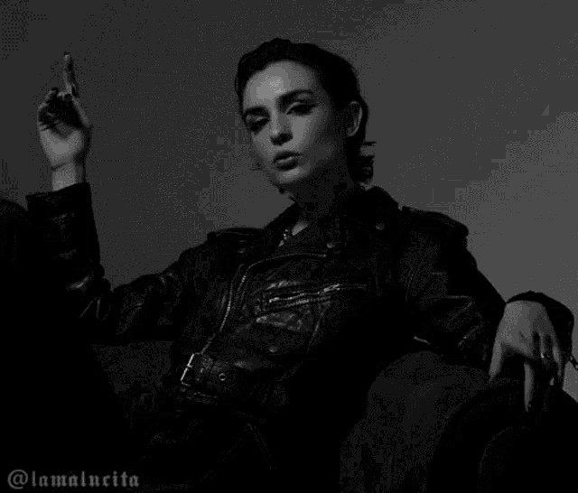 a woman in a leather jacket is sitting on a couch and giving the middle finger .