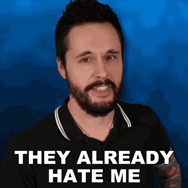 a man with a beard stands in front of a blue background with the words they already hate me