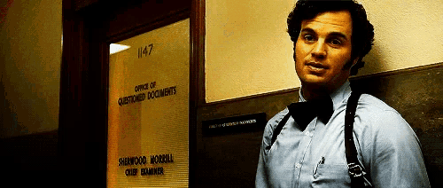 a man in a bow tie is standing in front of a door that says office of questioned documents