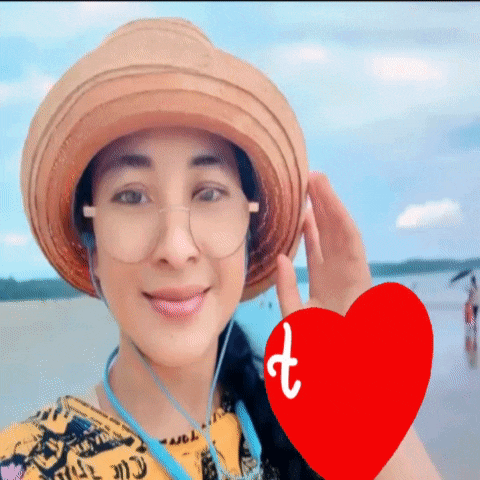 a woman wearing a hat and glasses is smiling with a red heart with the letter t on it