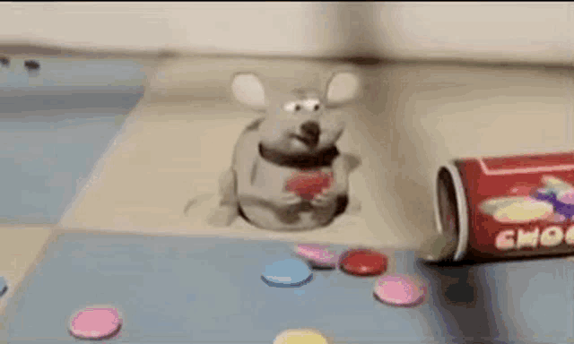 a cartoon mouse is sitting on a table next to a can of choco candy .