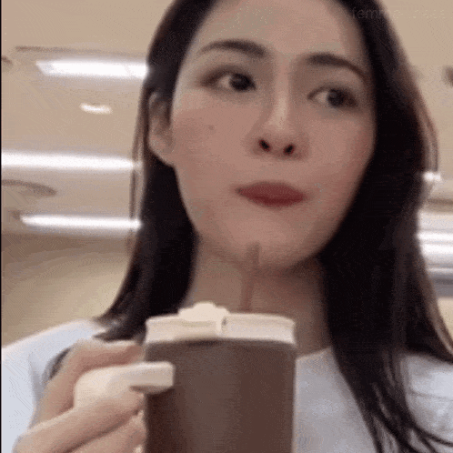 a woman is drinking from a cup with a straw in it .