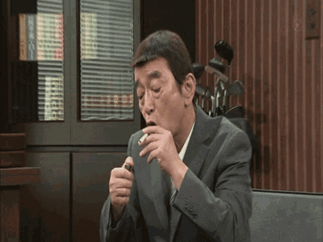 a man in a suit and tie is lighting a cigarette