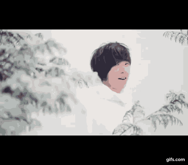 a young man in a white coat is standing in front of a tree .