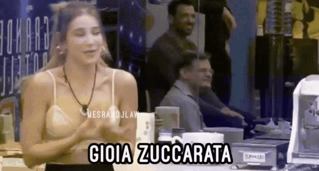 a woman in a white tank top is standing in front of a table with gioia zuccarata written on it .