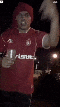 a man in a red shirt is holding a cup and says " e quem nao e "