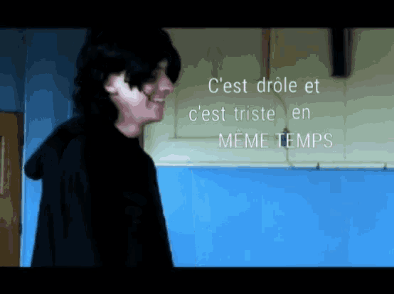 a man stands in front of a blue wall with the words " c'est drole et c'est triste en meme temps "