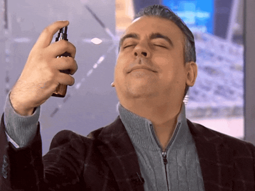 a man in a suit spraying something on his face with his eyes closed