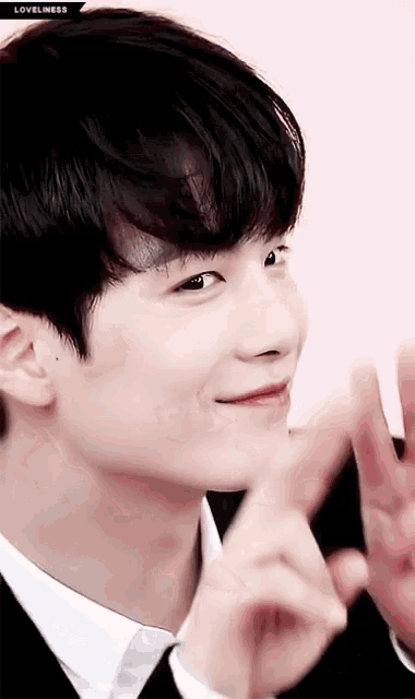 a close up of a young man in a suit and tie making a heart shape with his hands .