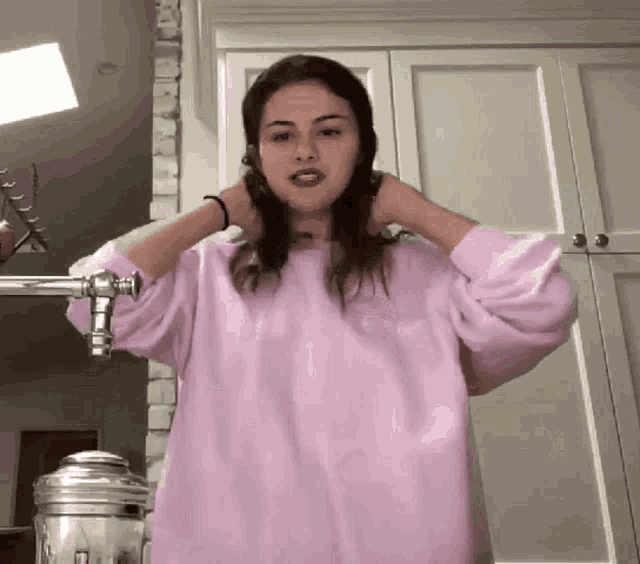 a woman wearing a pink sweatshirt is standing in front of a faucet