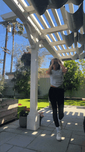 a woman is standing under a pergola with her hands on her head