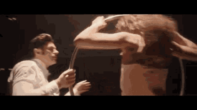 a man and a woman are standing next to each other in a dark room . the woman is wearing a red bra .