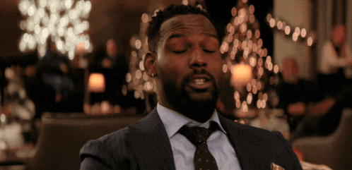 a man in a suit and tie is sitting in front of a christmas tree