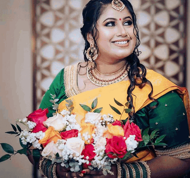 a woman wearing a yellow and green saree is holding a bouquet of flowers