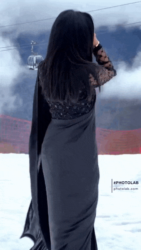 a woman in a black saree is standing in the snow with a ski lift in the background