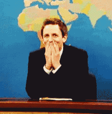 a man covering his mouth with his hands while sitting in front of a map of the world