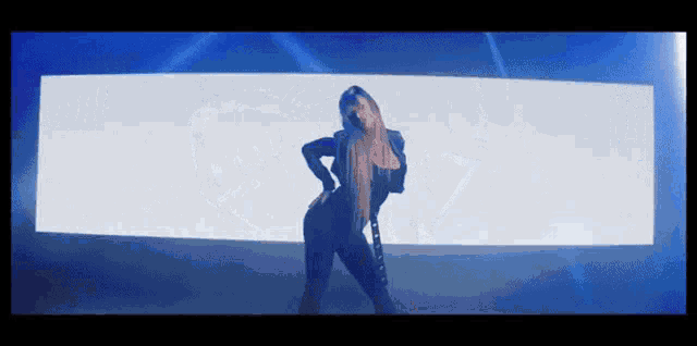 a woman in a black jumpsuit is dancing in front of a blue and white screen .