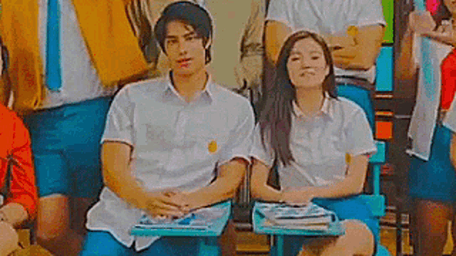a man and a woman are sitting at desks in a classroom with other students .