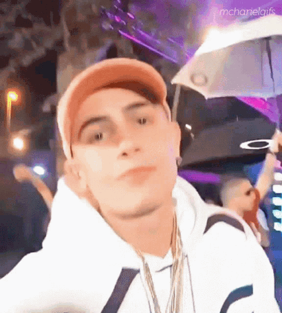 a man wearing a hat and holding an umbrella looks at the camera