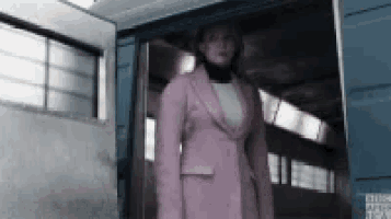 a woman in a pink suit stands in a doorway