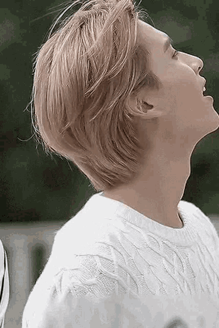 a young man with blonde hair is wearing a white sweater and looking up at the sky .